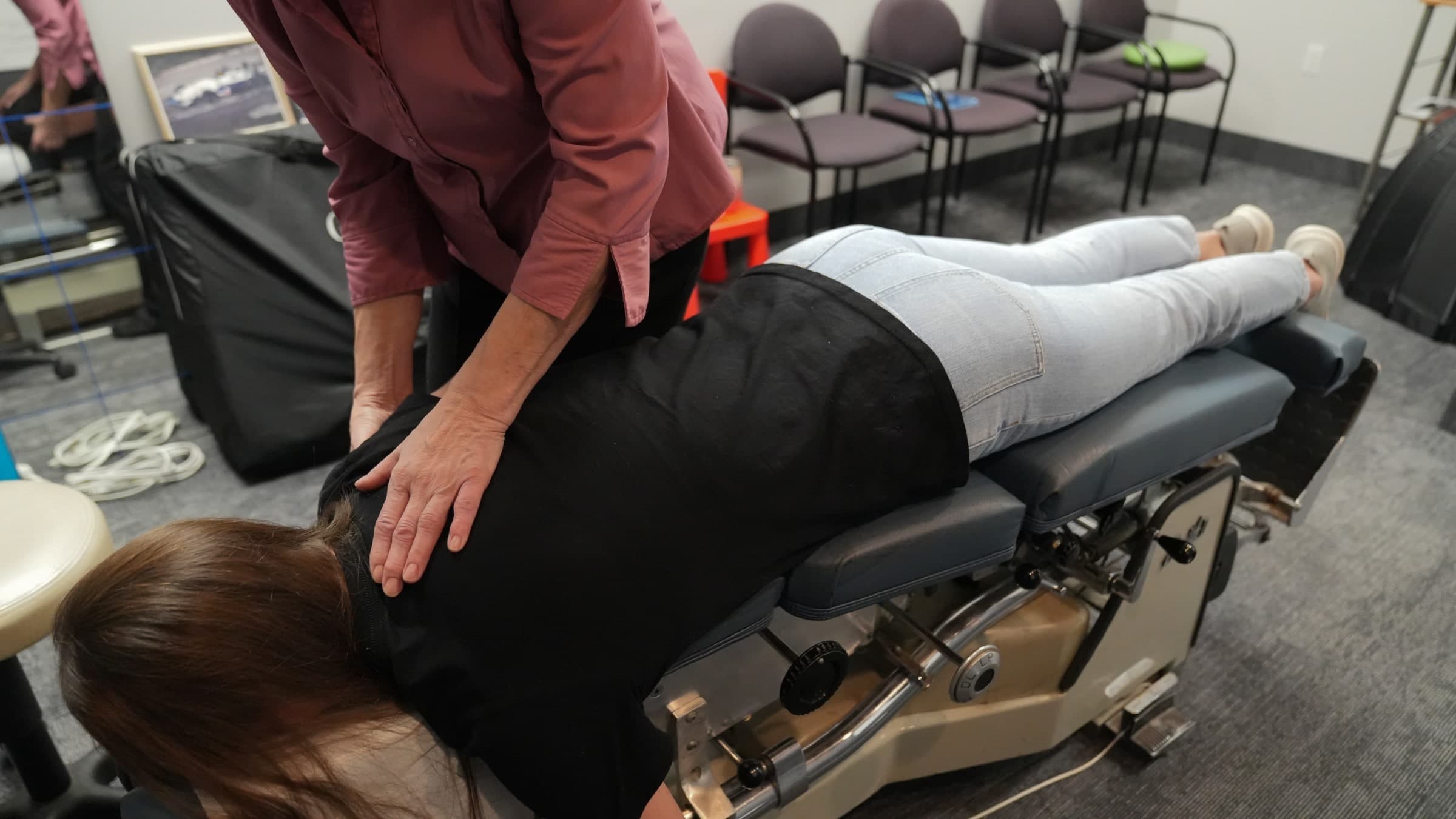 A chiropractor in a maroon shirt performs a spinal adjustment on a patient lying face-down on a treatment table at Life Chiropractic Centre in Burlington, Ontario