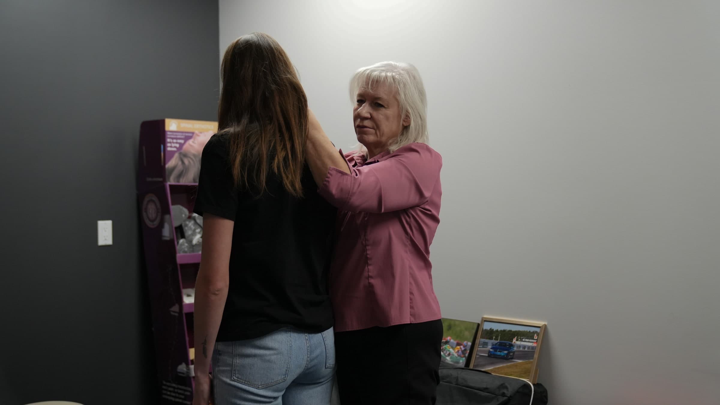 A chiropractor in a mauve shirt demonstrates a shoulder adjustment technique on a patient in a treatment room in Burlington, Ontario