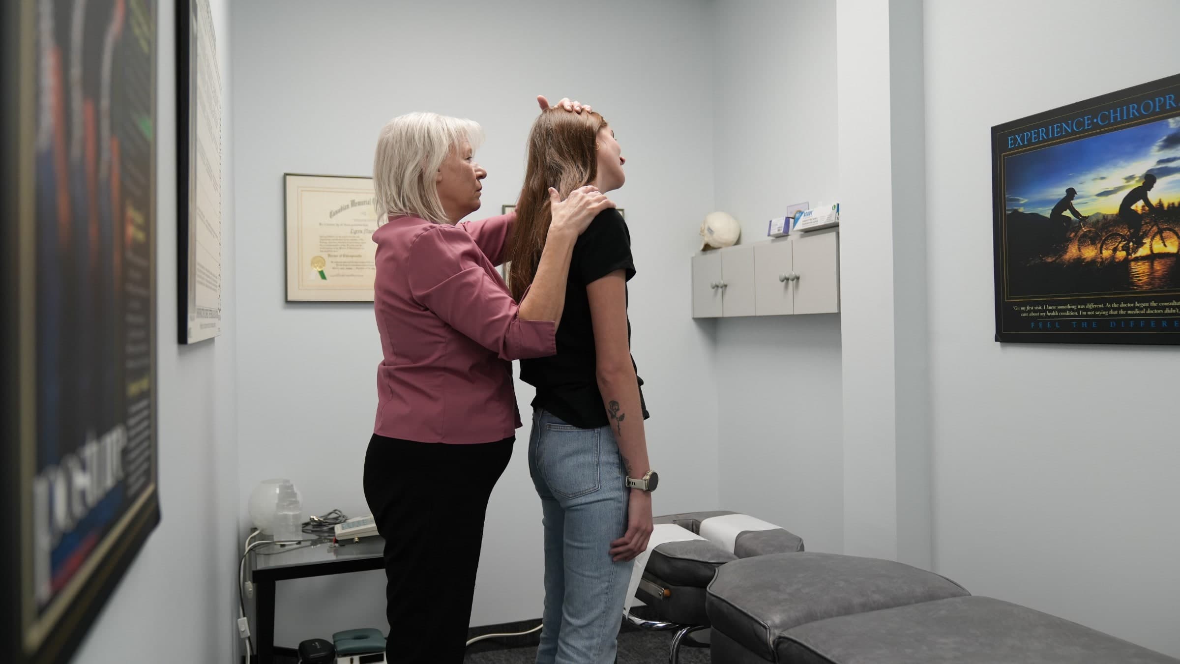 A chiropractor in a burgundy shirt performs a neck examination on a patient in a treatment room at Life Chiropractic Centre in Burlington, Ontario