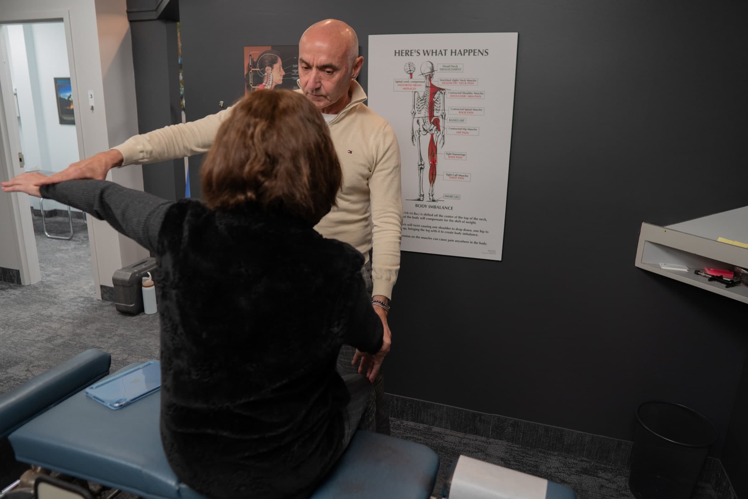 A chiropractor demonstrates a spinal anatomy diagram to a patient seated on an examination table at Life Chiropractic Centre in Burlington, Ontario