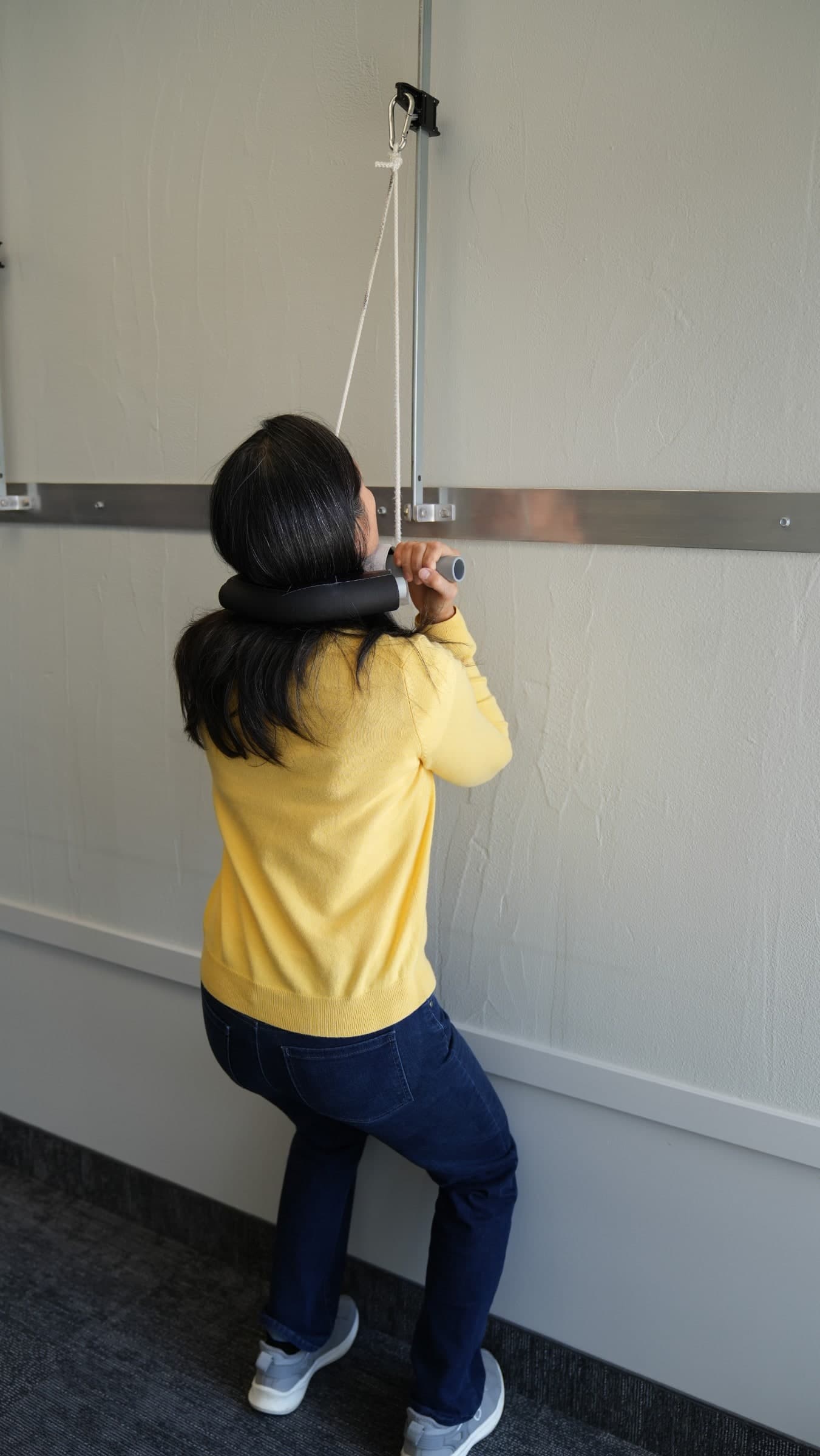 A person in a yellow sweater and dark hood performing a pull-up exercise on a suspended rope system mounted to a wall in Burlington