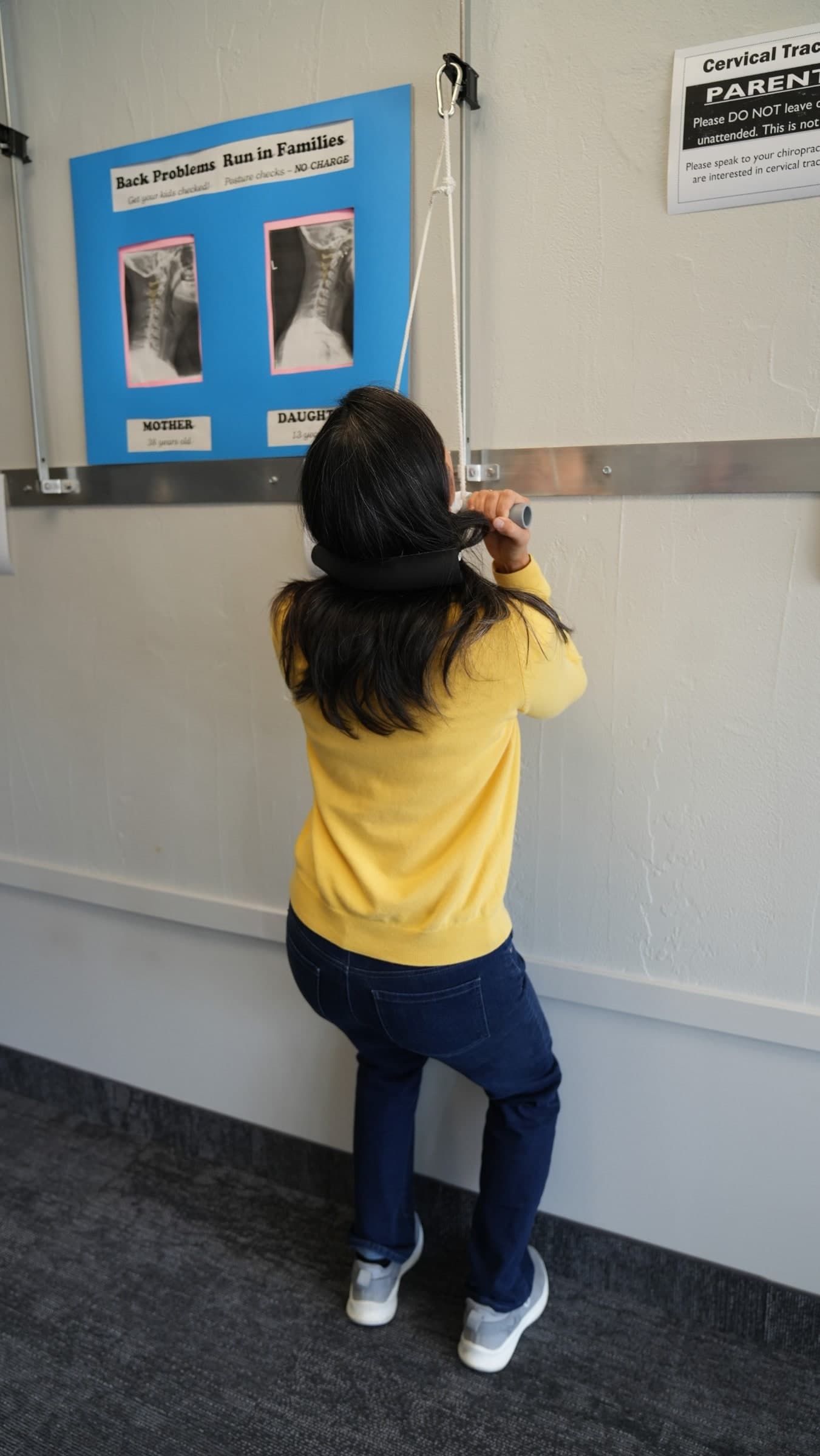 Child in yellow shirt and dark jeans viewing educational X-ray display about back problems in families at Burlington chiropractic clinic
