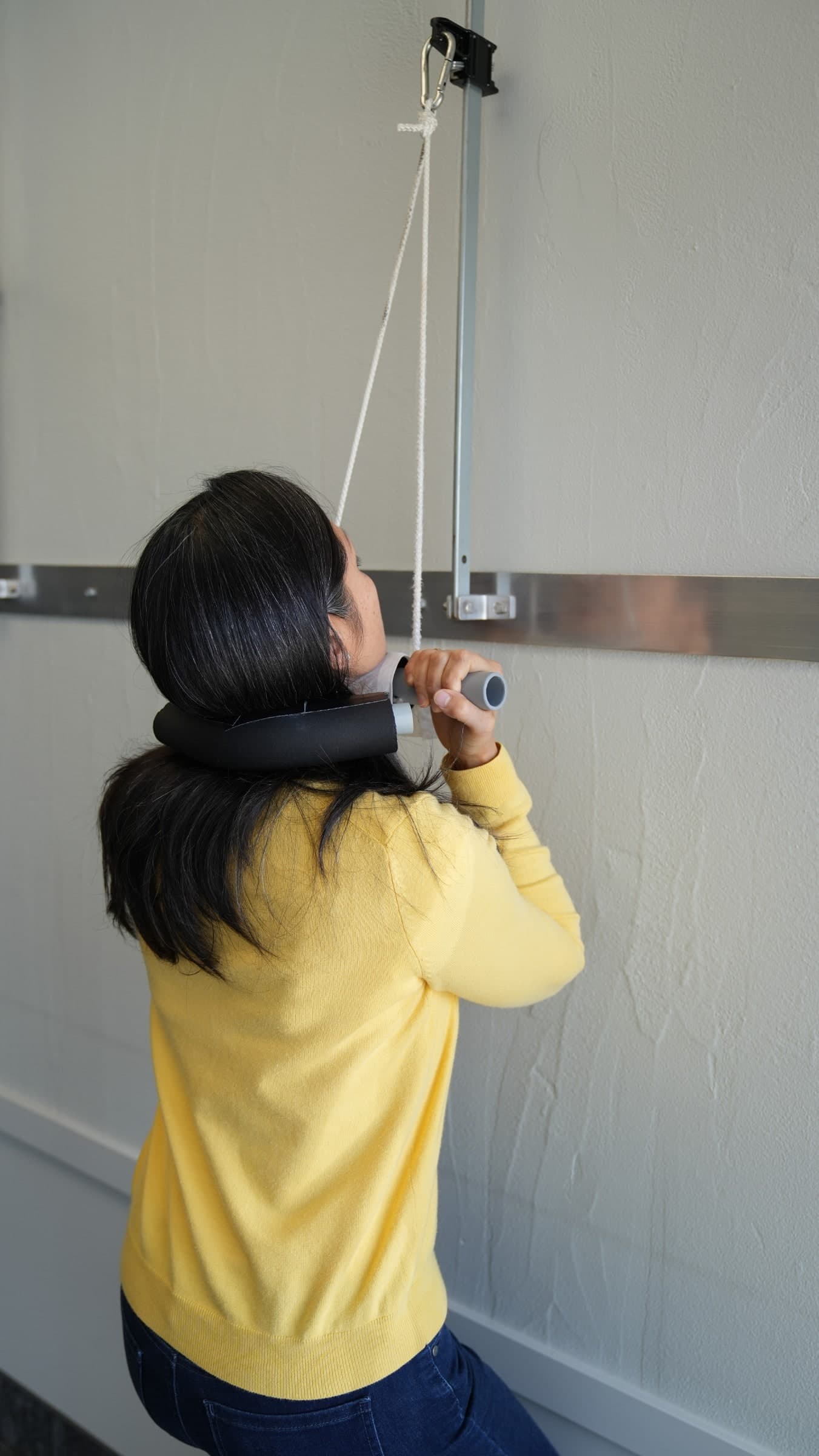 Child in yellow sweater and black neck brace pulling on a rope attached to a wall-mounted pulley system during an exercise or therapy session in Burlington